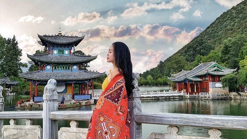 Tour Côn Minh - Đại Lý - Lệ Giang - Shangrila Từ Hà Nội 6n5đ Cô gái khoác khăn họa tiết đỏ đứng bên cầu đá trước lầu Đắc Nguyệt ở hồ Hắc Long Đầm Lệ Giang