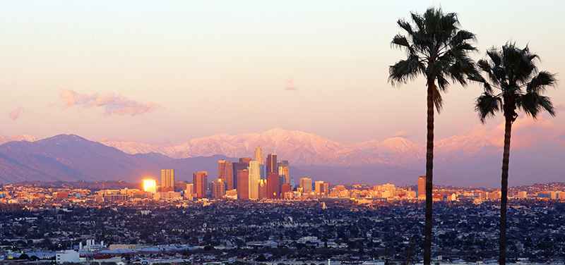 Đường chân trời Los Angeles và dãy núi phủ tuyết nhìn qua hai cây cọ lúc bình minh