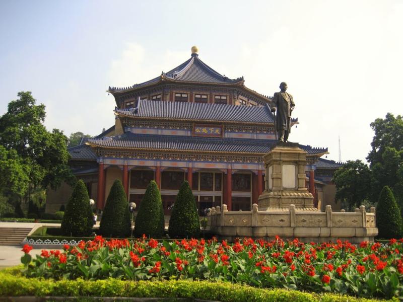 Tượng đài trước hội trường mái ngói xanh với vườn hoa đỏ ở Quảng Châu