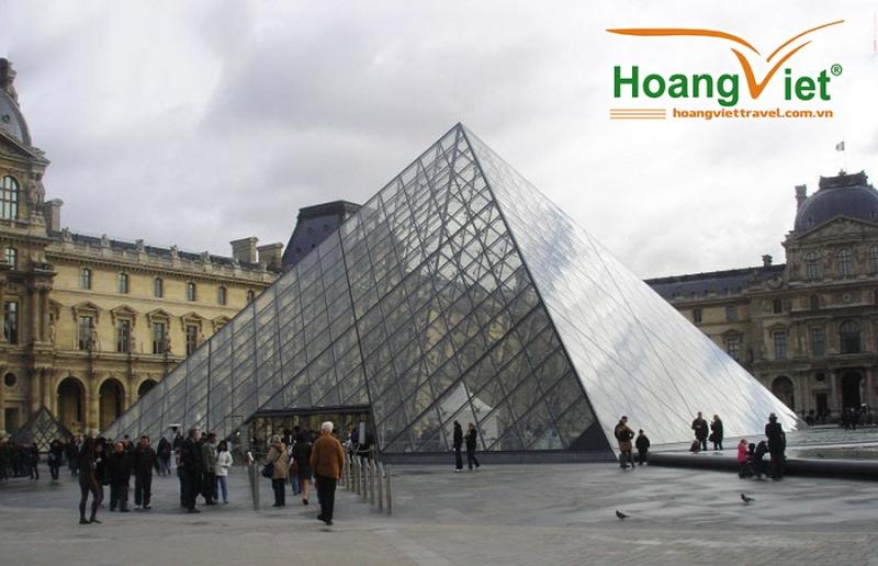 Kim tự tháp kính trước Bảo tàng Louvre với du khách đi lại trong sân