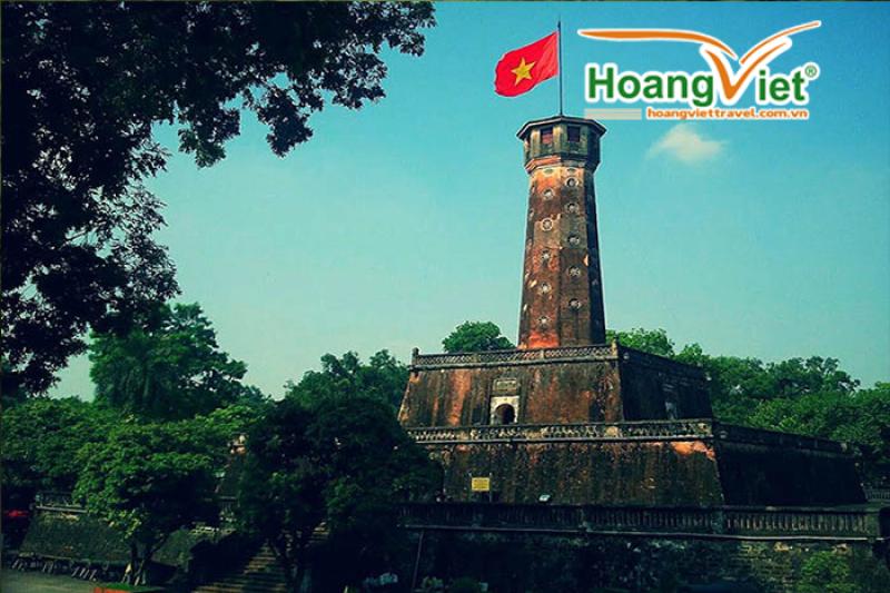Cột cờ Hà Nội với lá cờ đỏ sao vàng tung bay trên nền trời xanh giữa tán cây
