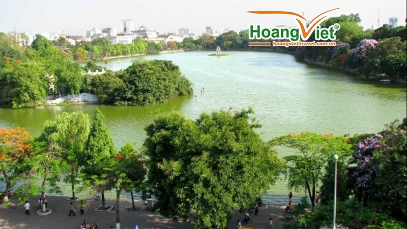 Toàn cảnh hồ Gươm xanh nhìn từ trên cao, xung quanh là hàng cây phượng và hoa tím rợp bóng.