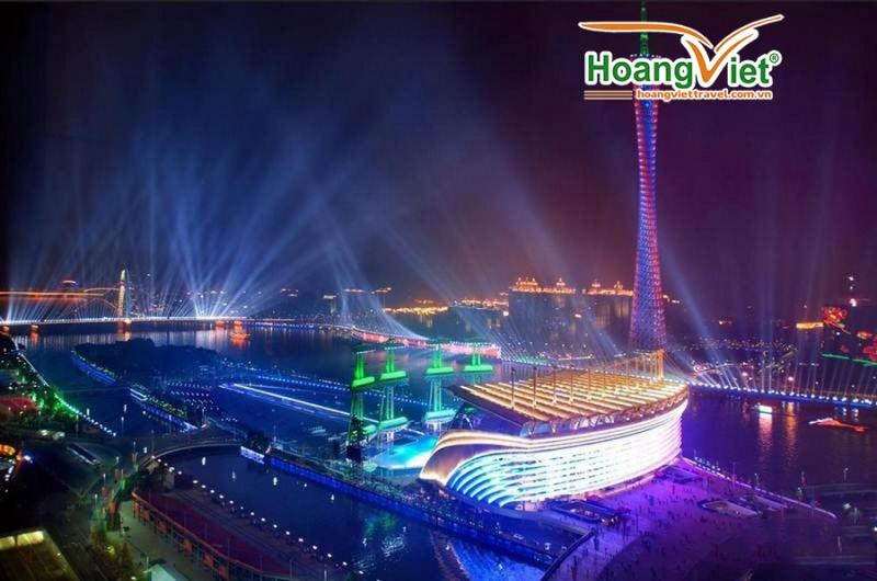 Tháp truyền hình và công trình bên sông lung linh ánh đèn, tia sáng chiếu lên bầu trời đêm.