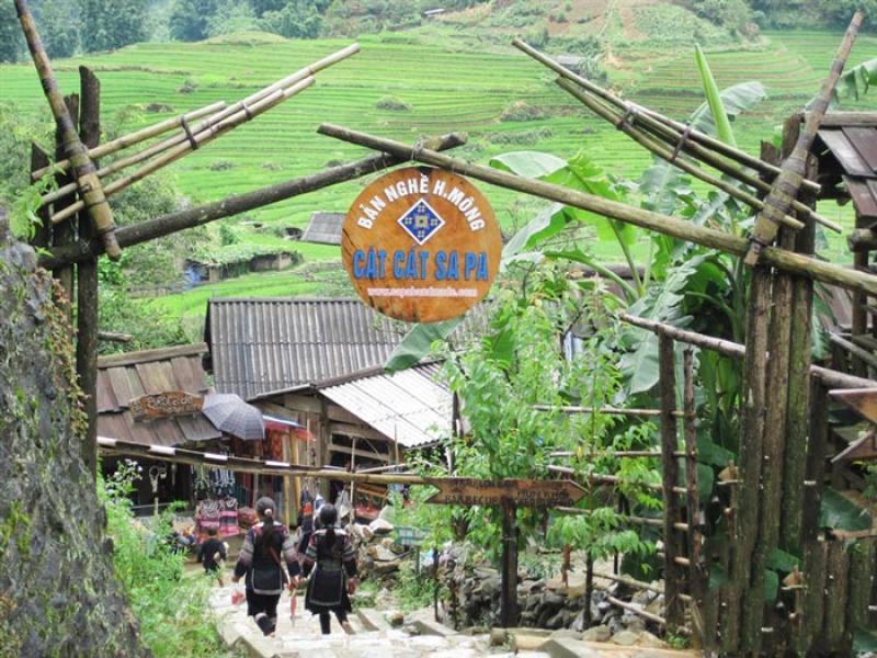 Cổng tre bản Cát Cát có biển gỗ tròn, hai người phụ nữ đi xuống bậc đá giữa ruộng bậc thang