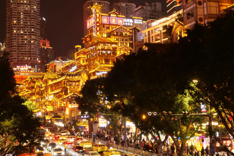 Cụm nhà gỗ cổ rực sáng đèn vàng về đêm ở Hồng Nhai Động, phía trước là dòng xe cộ.