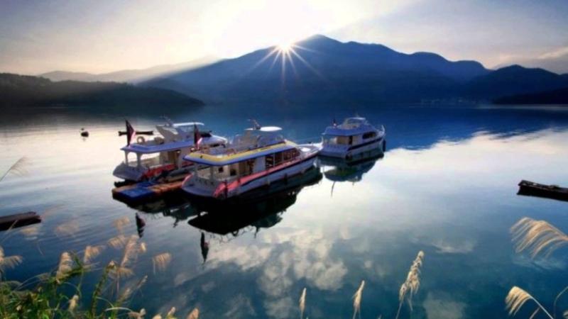Những du thuyền neo trên mặt hồ lúc bình minh, tia nắng lấp ló sau dãy núi