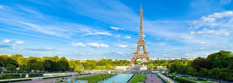 Tháp Eiffel cao vút giữa bầu trời xanh nhiều mây, phía trước là hồ nước và công viên xanh