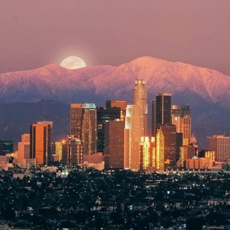Đường chân trời Los Angeles dưới dãy núi phủ tuyết với trăng tròn mọc lúc hoàng hôn