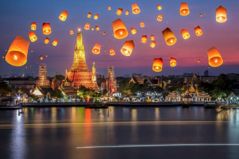 Nhiều chiếc đèn trời bay trên bầu trời hoàng hôn phía trên tháp Wat Arun bên sông