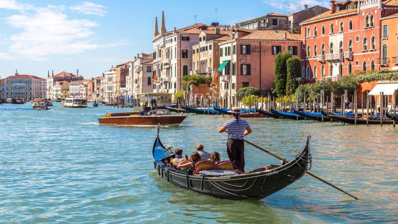 Người lái thuyền gondola chở du khách trên kênh đào lớn bên những dãy nhà cổ ở Venice