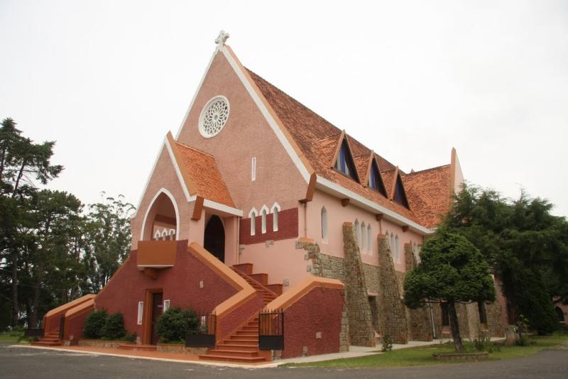 Nhà thờ Domaine de Marie màu hồng với mái ngói đỏ giữa hàng thông