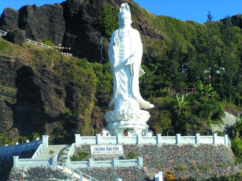 Tượng Quan Âm trắng trên bệ sen giữa sườn núi đá, phía dưới có biển Quan Âm Đài.