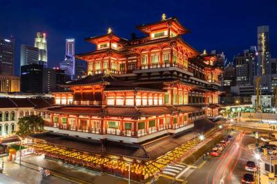 Ngôi chùa Phật giáo được chiếu sáng với kiến trúc truyền thống nổi bật trên nền đường chân trời thành phố hiện đại về đêm. Ánh sáng ấm áp, mời gọi; năng lượng đô thị nhộn nhịp.