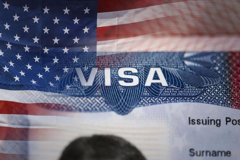 Ảnh cận cảnh một thị thực Hoa Kỳ với quốc kỳ Mỹ ở phía sau. Từ "VISA" được hiển thị nổi bật, tượng trưng cho việc đi lại và nhập cư.