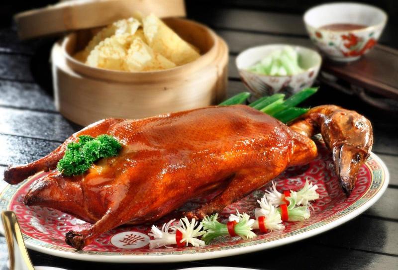 Vịt quay Bắc Kinh được bày trên đĩa trang trí đẹp mắt với rau mùi tây, ăn kèm với niêu tre, dưa chuột thái lát và nước chấm, gợi lên trải nghiệm ẩm thực truyền thống và thanh lịch.