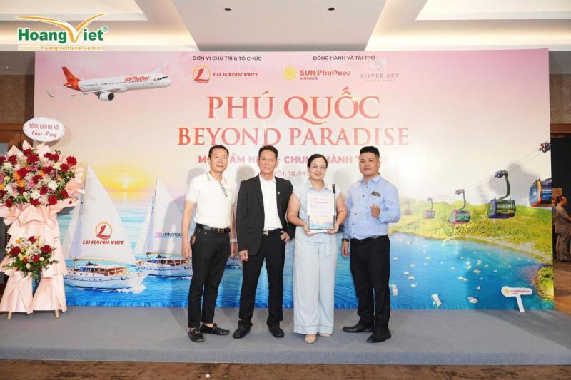 Bốn người đứng mỉm cười trước phông nền "Phú Quốc Beyond Paradise". Không khí hân hoan với hoa và các hình ảnh mang chủ đề du lịch.