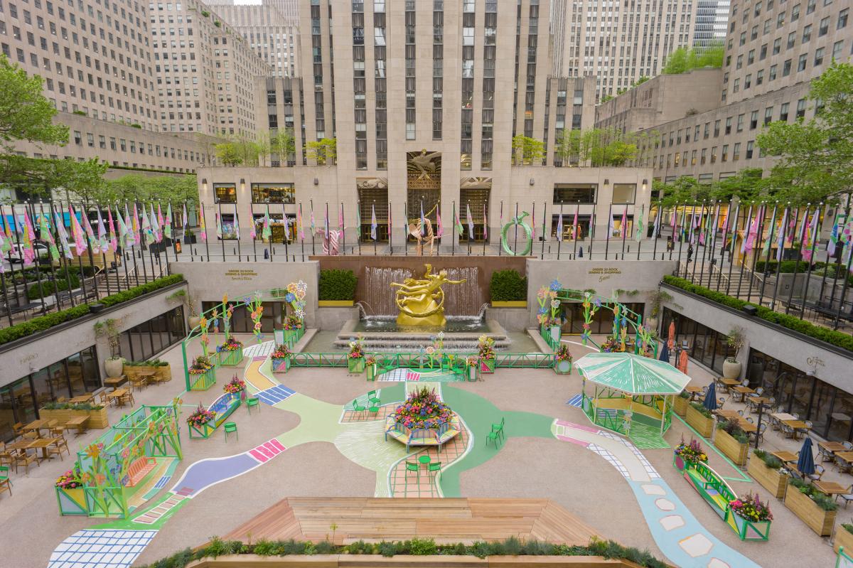 Toàn cảnh quảng trường Rockefeller Center nhìn từ trên cao, nổi bật với tác phẩm nghệ thuật sắp đặt đầy màu sắc, rực rỡ cùng hoa và lối đi. Cờ được treo dọc khu vực phía trên.