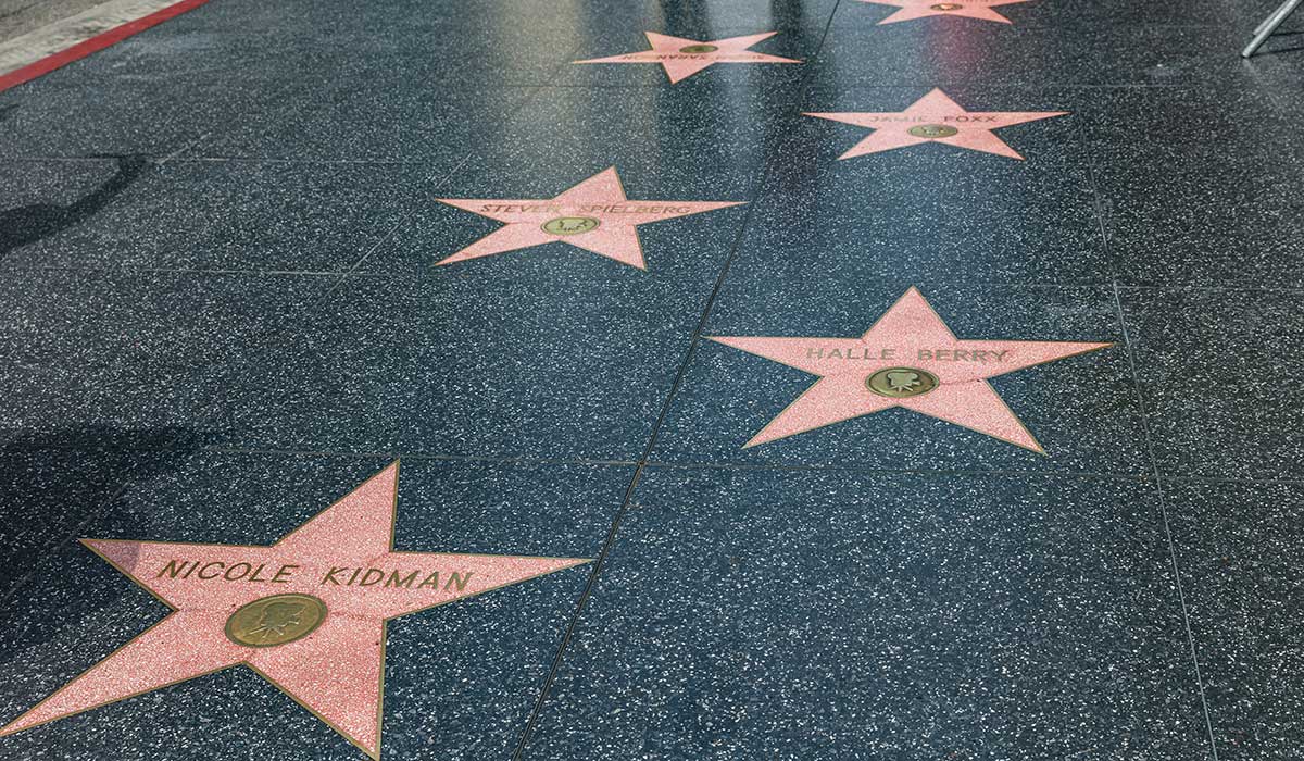 Vỉa hè với những ngôi sao màu hồng mang tên các nhân vật như Nicole Kidman và Halle Berry trên Đại lộ Danh vọng Hollywood, truyền tải cảm giác về sự nổi tiếng và thành tựu.
