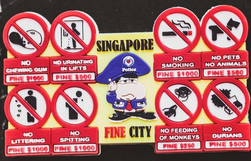 Lưu ý khi đi du lịch Singapore: Hình minh họa một viên cảnh sát hoạt hình nghiêm nghị có nhãn "Thành phố Singapore xinh đẹp" xung quanh là các biển báo: Cấm nhai kẹo cao su, tiểu tiện, xả rác, khạc nhổ, hút thuốc, nuôi thú cưng, cho khỉ ăn và cấm ăn sầu riêng, mỗi hành vi đều bị phạt tiền.