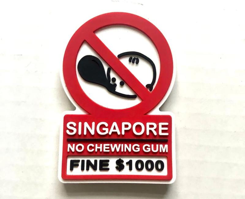 Biển báo màu đỏ trắng có hình biểu tượng kẹo cao su bị cấm kèm dòng chữ: "Singapore Cấm nhai kẹo cao su, phạt 1000 đô la Singapore." Thể hiện quy định nghiêm ngặt.