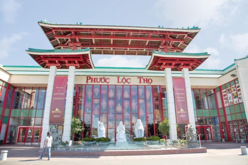 Hình ảnh cho thấy lối vào trung tâm mua sắm Phước Lộc Thọ, mang phong cách kiến trúc truyền thống Á Đông với điểm nhấn màu đỏ và xanh lá cây, cùng ba bức tượng trắng phía trước.