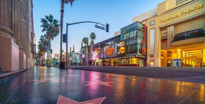 Đại lộ Hollywood lúc hoàng hôn, với những ngôi sao trên Đại lộ Danh vọng, quán Hard Rock Cafe rực rỡ ánh đèn neon, những hàng cây cọ và mặt tiền nhà hát Dolby được chiếu sáng.