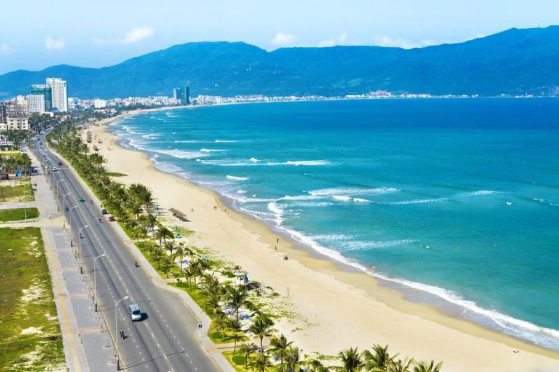 Bãi biển Mỹ Khê với bờ cát dài, hàng dừa, con đường ven biển và dãy núi phía xa.