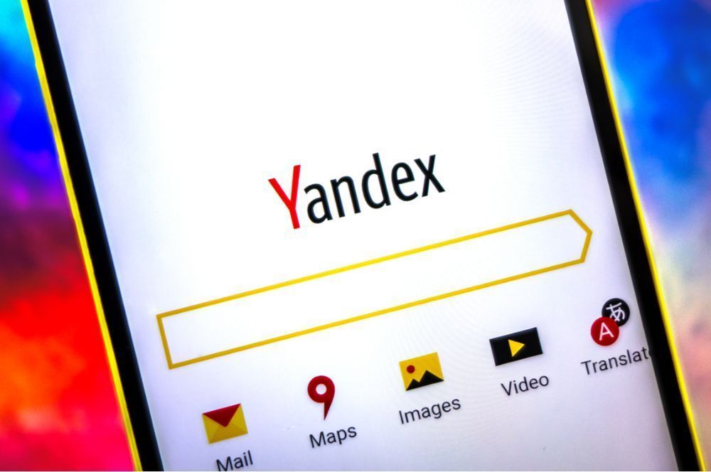 Ảnh cận cảnh một chiếc điện thoại thông minh hiển thị trang chủ Yandex. Màn hình hiển thị thanh tìm kiếm và các biểu tượng cho Thư, Bản đồ, Hình ảnh, Video và Dịch thuật, trên nền màu sắc mờ ảo.