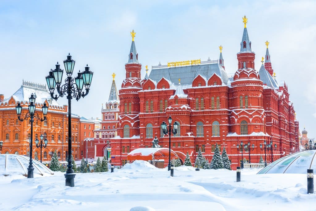 Tòa nhà gạch đỏ cổ kính ở Quảng trường Đỏ, Moscow, phủ đầy tuyết. Những cột đèn đường và cây cối trang nhã tạo nên sự tương phản dưới bầu trời trong xanh, rực rỡ.