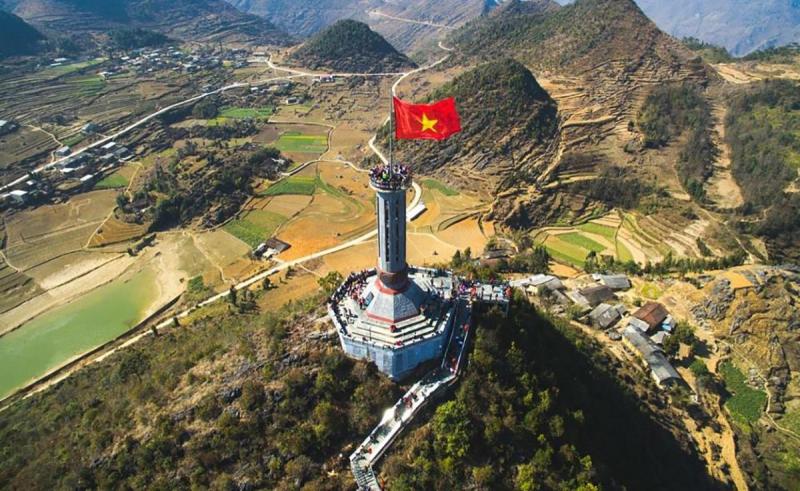Cột cờ Lũng Cú với lá cờ đỏ sao vàng trên đỉnh núi, nhìn từ trên cao xuống ruộng bậc thang