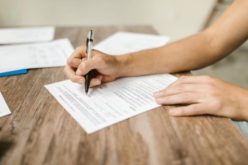 Người dùng bút điền biểu mẫu giấy tờ, minh họa bước hoàn thiện đơn xin visa Ý.