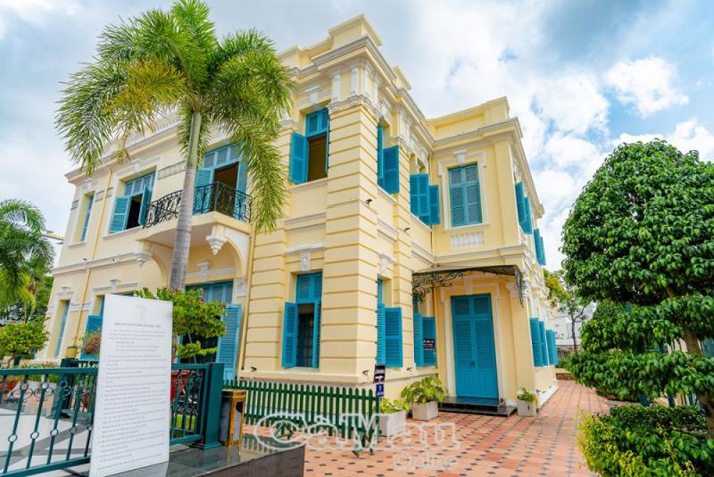 Tòa nhà hai tầng màu vàng với cửa chớp xanh và hàng cây cọ trong khuôn viên nhà Công tử Bạc Liêu.
