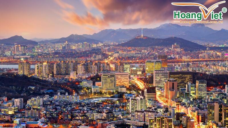 Toàn cảnh Seoul lúc hoàng hôn, tháp Namsan trên đồi giữa biển nhà cao tầng và núi.