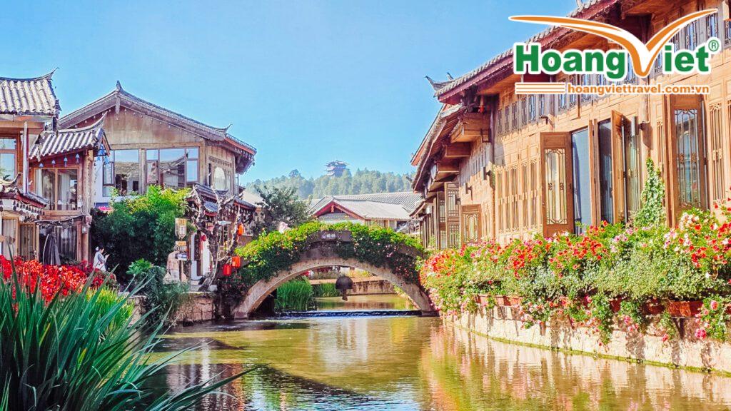 Kiến trúc truyền thống Trung Hoa nằm dọc theo một con kênh yên tĩnh, được tô điểm bởi những bông hoa và cây xanh rực rỡ. Một cây cầu đá uốn cong duyên dáng ở giữa.