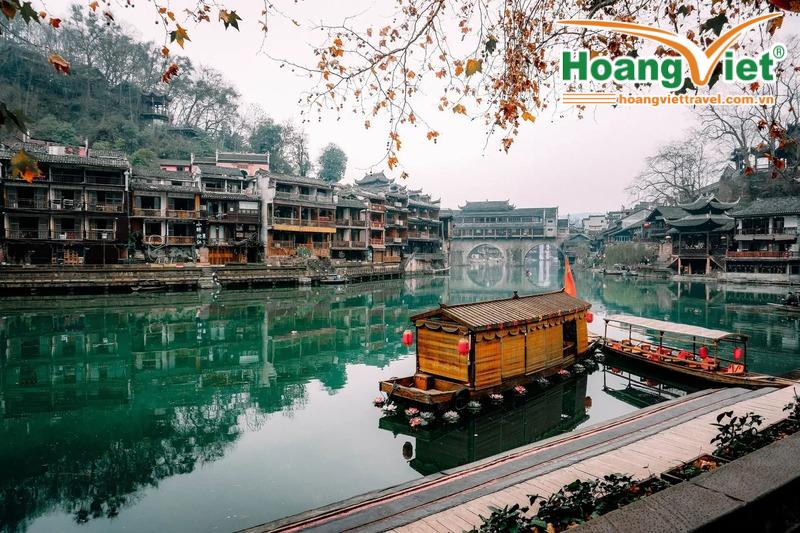 Những chiếc thuyền gỗ truyền thống nhẹ nhàng trôi trên dòng sông xanh ngọc êm đềm, hai bên là những công trình kiến ​​trúc cổ kính của Trung Hoa. Lá mùa thu rụng xuống càng làm tăng thêm vẻ thanh bình.