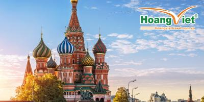 Cảnh tượng Nhà thờ Thánh Basil rực rỡ sắc màu ở Moscow dưới ánh nắng mặt trời, với những mái vòm hình củ hành đầy màu sắc, được bao quanh bởi cây cối và bầu trời trong xanh với những đàn chim bay lượn, tạo nên một bầu không khí thanh bình.