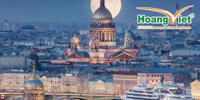 Trăng tròn tỏa sáng phía sau một nhà thờ lớn được thắp sáng rực rỡ giữa khung cảnh thành phố rộng lớn. Một du thuyền neo đậu gần những tòa nhà trang trí công phu bên bờ sông, toát lên vẻ sang trọng.