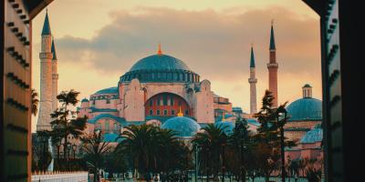 Thánh đường Hagia Sophia ở Istanbul nhìn qua vòm cửa với lối đi lát đá, hàng cây và các ngọn tháp dưới hoàng hôn