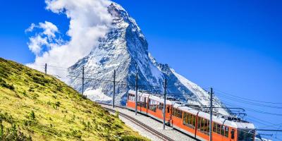 Đoàn tàu đỏ chạy trên sườn đồi cỏ với đỉnh Matterhorn phủ tuyết phía sau Đoàn tàu đỏ chạy trên sườn đồi cỏ với đỉnh Matterhorn phủ tuyết phía sau