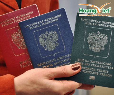 Một bàn tay đang cầm ba loại giấy tờ của Liên bang Nga: hộ chiếu màu đỏ, giấy thông hành màu xanh lam và giấy phép cư trú màu xanh lá cây dành cho người không quốc tịch.
