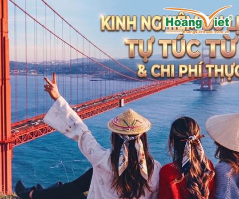 Ba người đội nón truyền thống Việt Nam đứng đối diện cầu Cổng Vàng lúc hoàng hôn, một người giơ biểu tượng hòa bình.