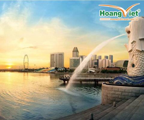 Cảnh hoàng hôn trên vịnh Marina với bức tượng Merlion phun nước nổi tiếng ở phía trước. Đường chân trời nổi bật với những tòa nhà hiện đại và vòng đu quay.