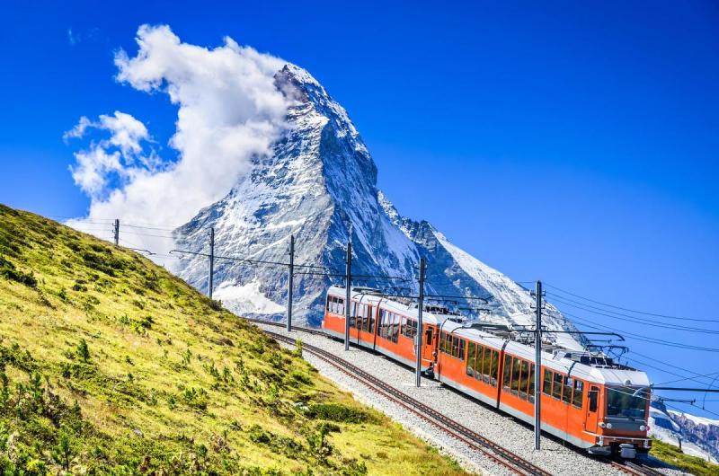 Đoàn tàu đỏ chạy trên sườn đồi cỏ với đỉnh Matterhorn phủ tuyết phía sau Đoàn tàu đỏ chạy trên sườn đồi cỏ với đỉnh Matterhorn phủ tuyết phía sau