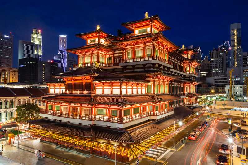 Ngôi chùa Phật giáo được chiếu sáng với kiến ​​trúc truyền thống nổi bật trên nền đường chân trời thành phố hiện đại về đêm. Ánh sáng ấm áp, mời gọi; năng lượng đô thị nhộn nhịp.