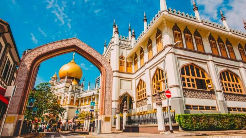 Thánh đường Hồi giáo Sultan lịch sử với mái vòm vàng lớn và kiến trúc trang trí công phu dưới bầu trời xanh trong vắt, được bao quanh bởi một cổng vòm phức tạp và con phố nhộn nhịp.