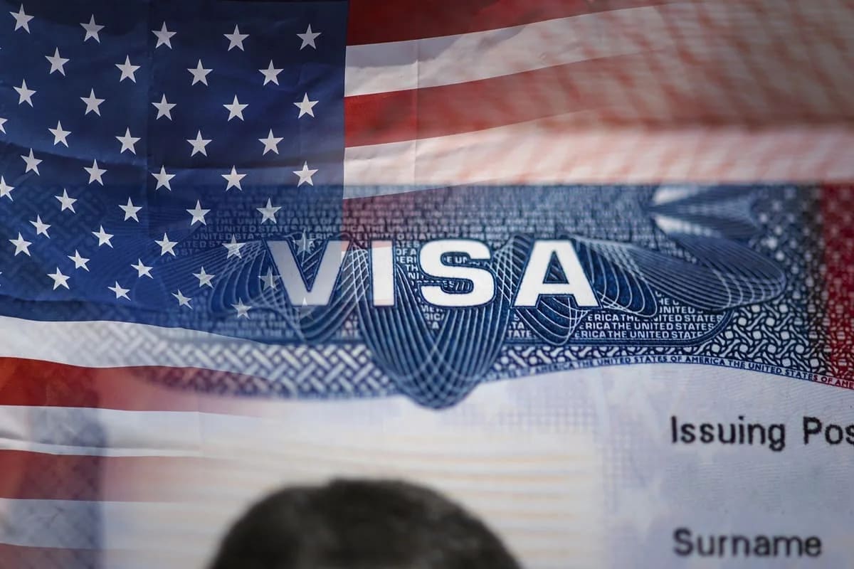 Ảnh cận cảnh một thị thực Hoa Kỳ với quốc kỳ Mỹ ở phía sau. Từ "VISA" được hiển thị nổi bật, tượng trưng cho việc đi lại và nhập cư.