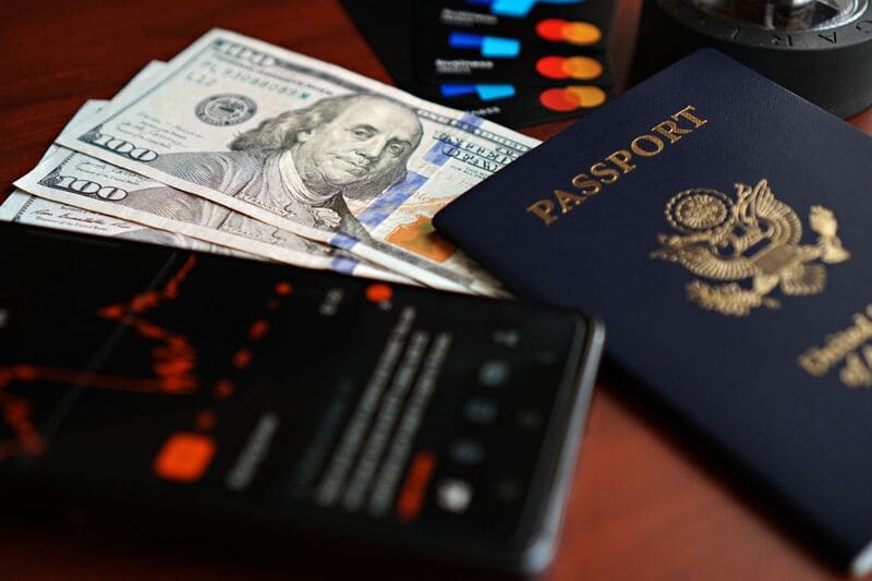 Tiền mặt 100 USD, thẻ ngân hàng và hộ chiếu cần chuẩn bị khi đi du lịch Mỹ đặt trên bàn gỗ
