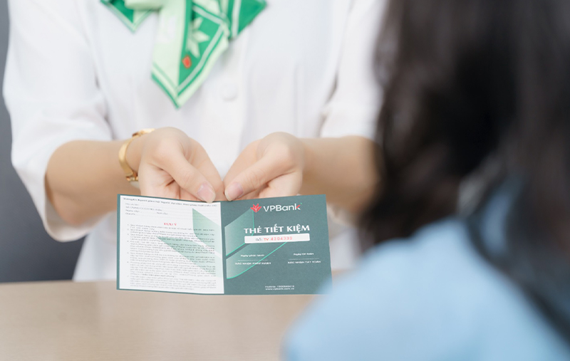 Nhân viên ngân hàng VPBank trao thẻ tiết kiệm màu xanh cho khách hàng tại quầy giao dịch