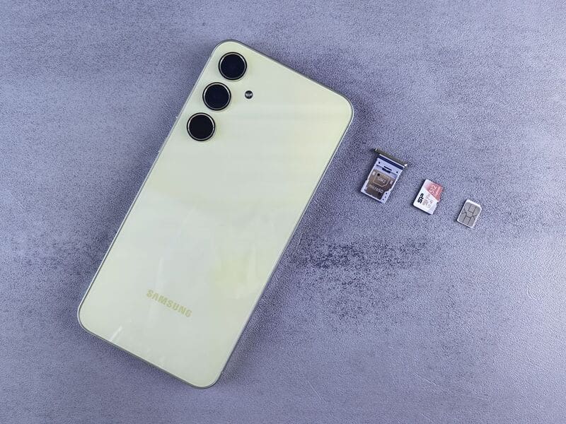 Điện thoại màu vàng chanh đặt bên cạnh khay SIM, thẻ nhớ MicroSD và thẻ SIM trên nền xám