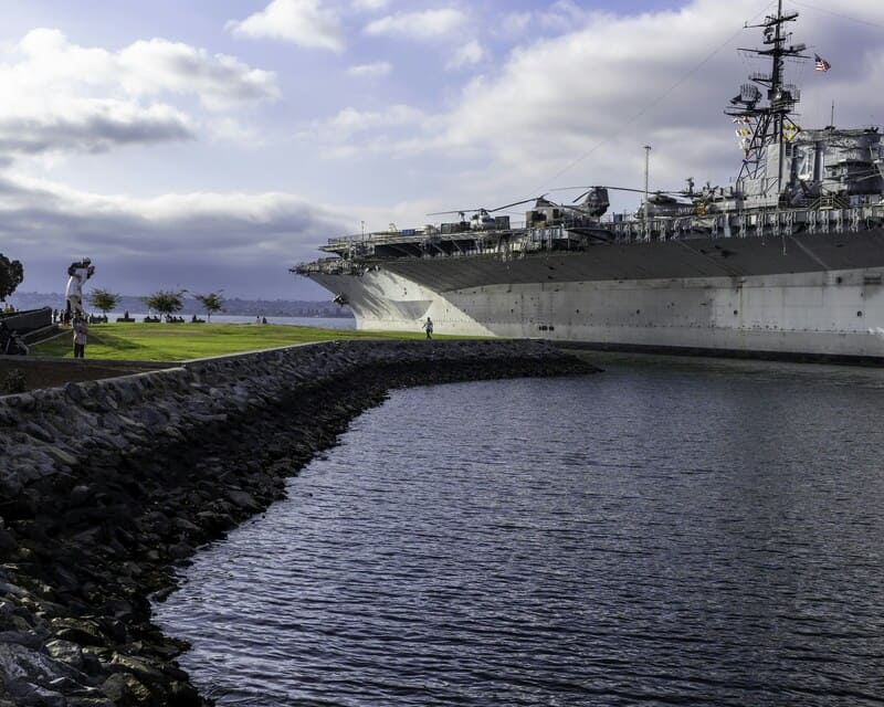 Tàu sân bay USS Midway với các trực thăng trên boong neo đậu cạnh bờ kè đá và công viên
